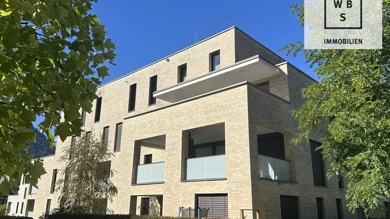 Modernes Mehrfamilienhaus mit heller Klinkerfassade und Balkonen unter blauem Himmel.