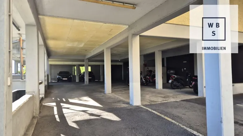 Überdachter Parkplatzbereich mit Betonpfeilern und Stellplätzen für Autos und Motorroller.