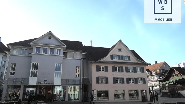 Historische Gebäude mit Geschäften im Erdgeschoss und Wohnungen darüber unter blauem Himmel.