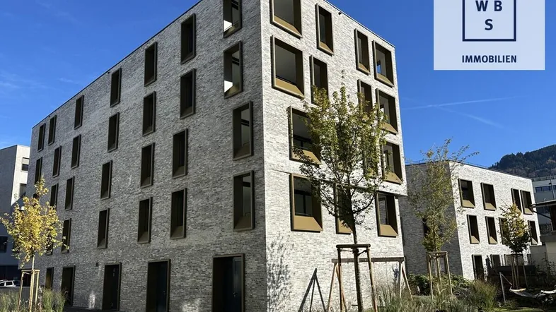 Modernes Mehrfamilienhaus mit heller Ziegelfassade und großen Fenstern in einer grünen Umgebung.