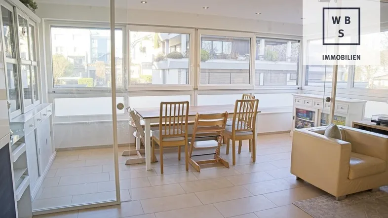 Heller Wohn- und Essbereich mit großen Fenstern, Fliesenboden und Zugang zu einem Balkon.