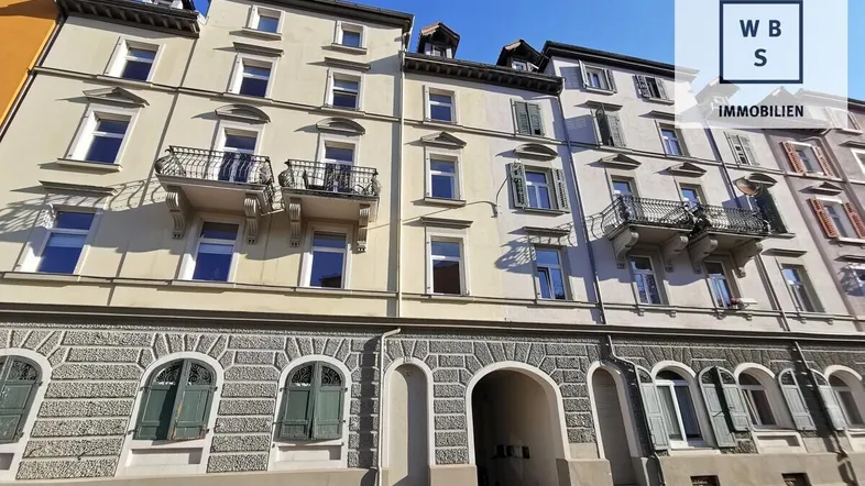 Historisches Mehrfamilienhaus mit klassischer Fassade, Balkonen und einem Torbogen im Erdgeschoss.