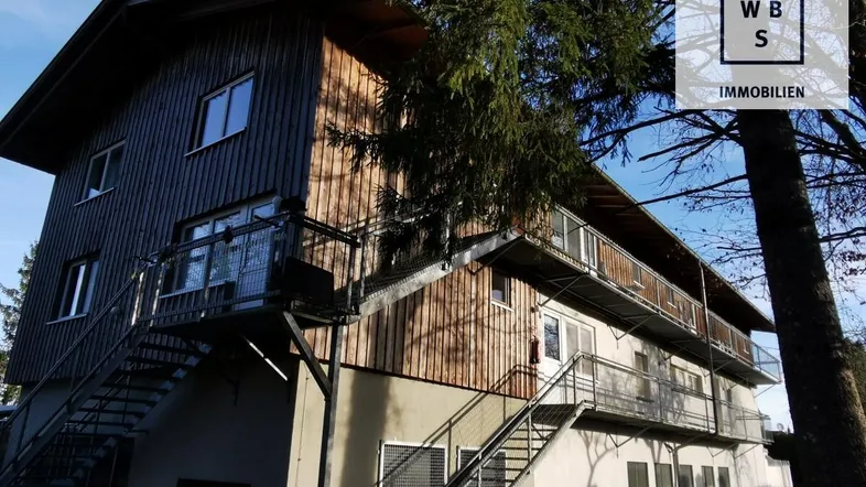 Mehrstöckiges Gebäude mit Holzverkleidung und mehreren Balkonen, umgeben von Bäumen.