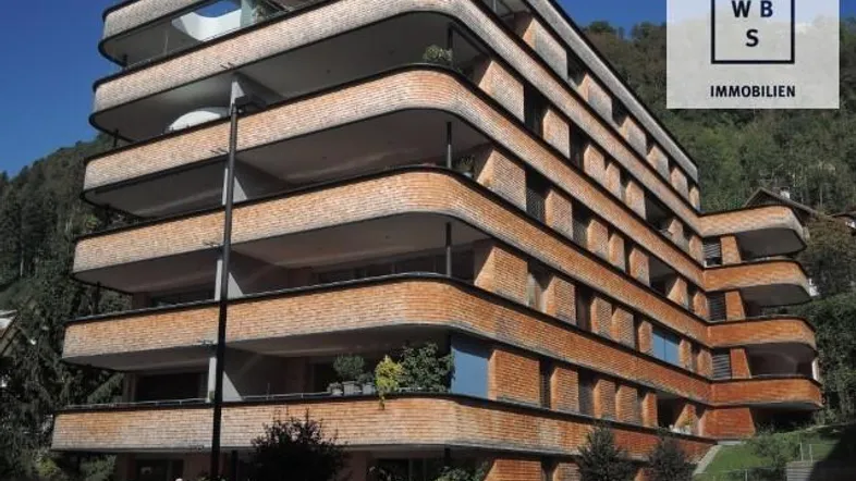 Modernes Mehrfamilienhaus mit geschwungenen Balkonen und einer Fassade aus Holz und Ziegeln.