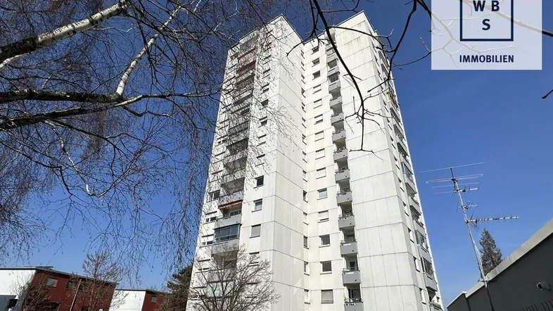 Hohes Wohngebäude mit vielen Etagen und Balkonen unter blauem Himmel.