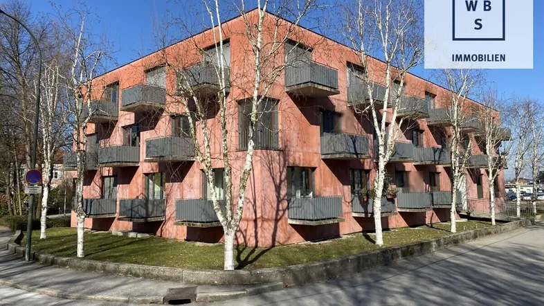 Modernes Mehrfamilienhaus mit markanter roter Fassade und zahlreichen Balkonen unter blauem Himmel.