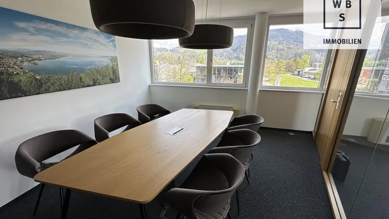Moderner Konferenzraum mit großem Holztisch, bequemen Stühlen und weitem Blick auf Berge und See.