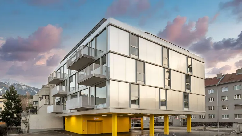 Modernes Wohngebäude mit Balkonen und gelbem Eingangsbereich unter einem dramatischen Himmel.
