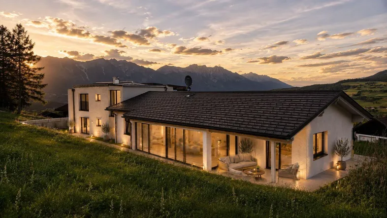 Modernes Wohnhaus in Hanglage mit weitem Blick auf die umliegende Berglandschaft bei Sonnenuntergang.