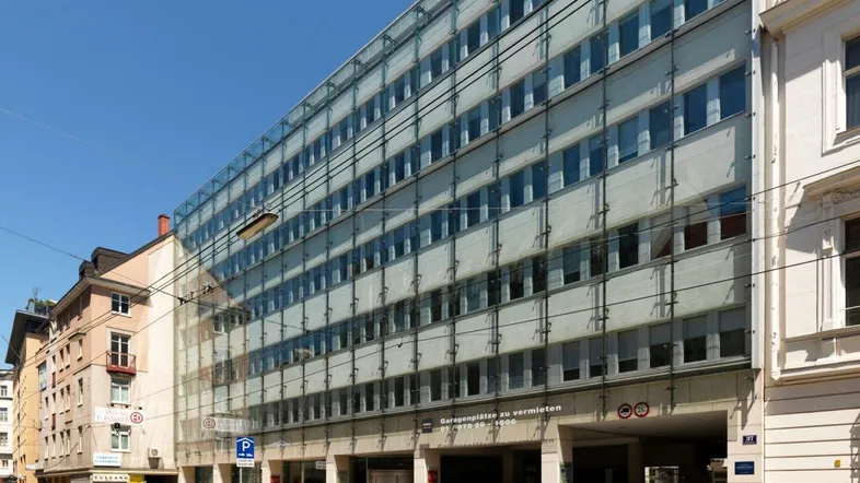 Modernes Geschäftsgebäude mit Glasfassade und integrierter Tiefgarage an einer belebten Straße in der Stadt.