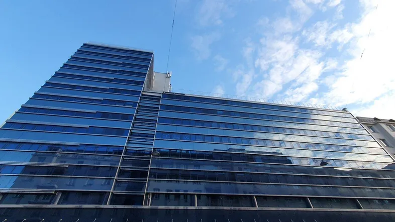 Modernes Bürogebäude mit blauer Glasfassade unter klarem Himmel und Wolken.