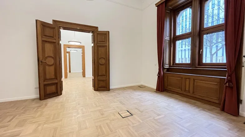 Geräumiger Raum mit Fischgrätparkett, hohen Decken und großen Holzfenstern in einem historischen Gebäude.