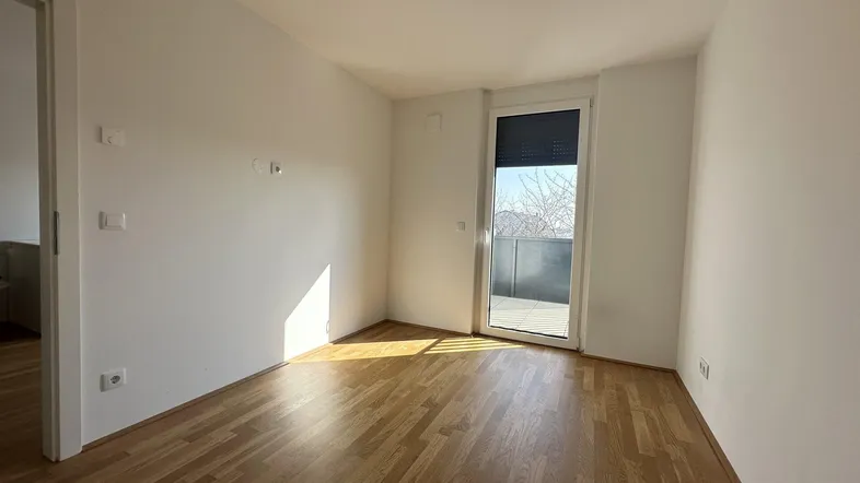 Helles Zimmer mit Parkettboden und Zugang zu einem Balkon, ideal als Schlafzimmer nutzbar.