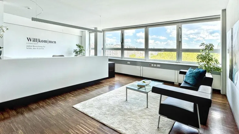 Heller Empfangsbereich mit Holzboden, großen Fenstern und moderner Einrichtung, ideal für Büroräume.