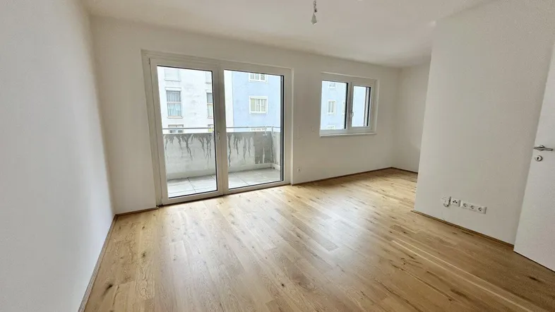 Heller Raum mit Parkettboden und Zugang zu einem Balkon, ideal als Wohnzimmer nutzbar.