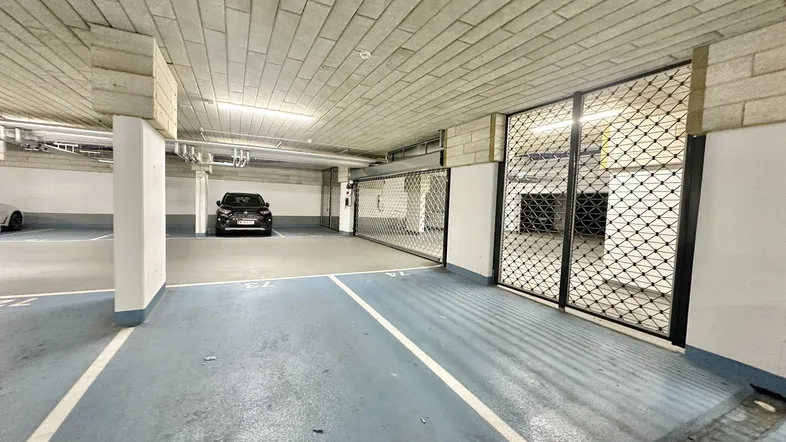 Tiefgarage mit markierten Parkplätzen und einem schwarzen Fahrzeug, durch Gittertore abgetrennt.