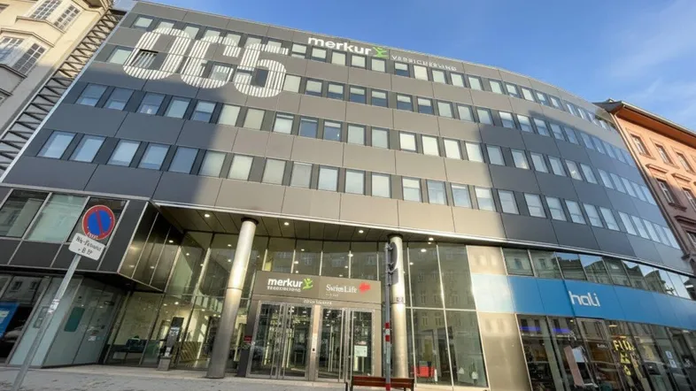 Modernes Bürogebäude mit Glasfassade und Firmenlogos, gelegen an einer belebten Straße.