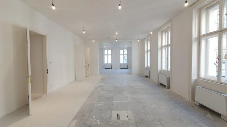 Großer, heller Raum mit vielen Fenstern und Betonboden, bereit für den Innenausbau.