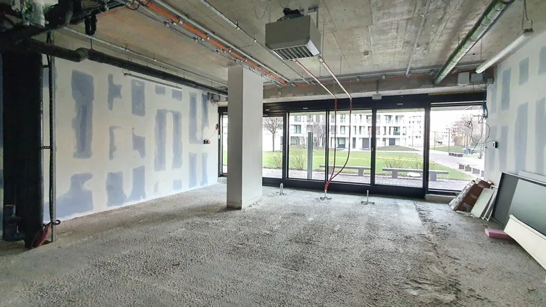 Großer, unfertiger Innenraum mit Betonboden und unverputzten Wänden, großen Fenstern und Blick ins Grüne.