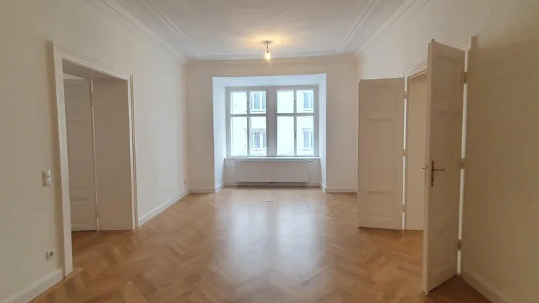 Geräumiger Raum mit Fischgrätparkett, hohen Decken und großen Fenstern, der viel natürliches Licht bietet.