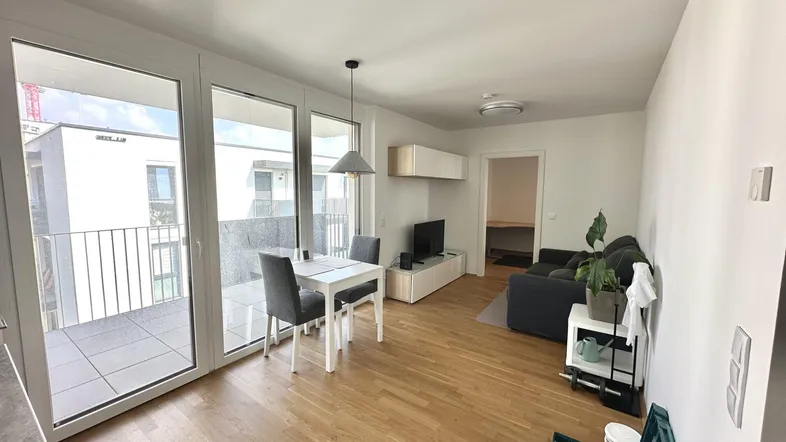 Heller Wohn- und Essbereich mit Parkettboden und Zugang zu einem sonnigen Balkon.