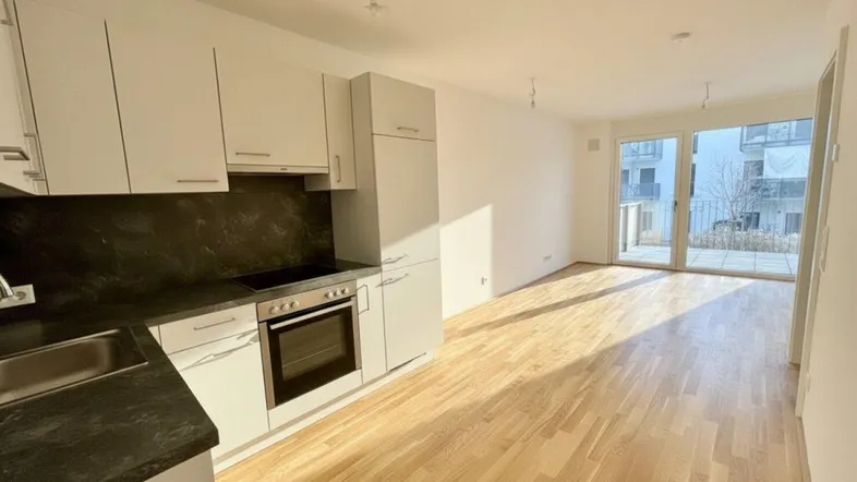 Helle, moderne Küche mit weißen Schränken, dunkler Arbeitsplatte und Zugang zum Balkon.