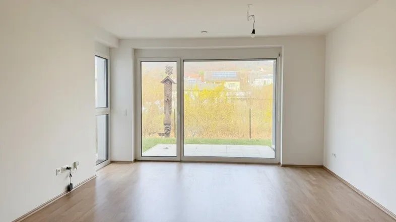 Heller, leerer Raum mit Holzboden und großer Glasschiebetür, die Zugang zu einem Außenbereich bietet.
