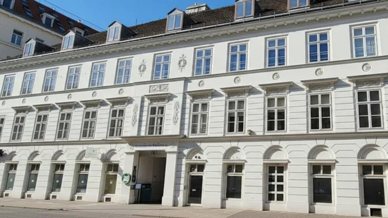 Historisches Gebäude mit weißer Fassade, vielen Fenstern und Dachgauben, gelegen an einer städtischen Straße.