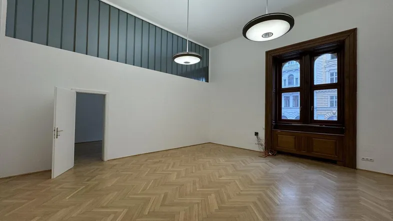 Geräumiger Raum mit Fischgrätparkett, hohen Decken und großen Fenstern mit Holzrahmen.