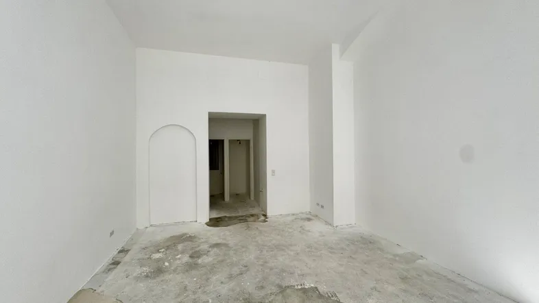 Leerer Raum mit weißen Wänden und Betonboden, bereit für den Ausbau und die individuelle Gestaltung.