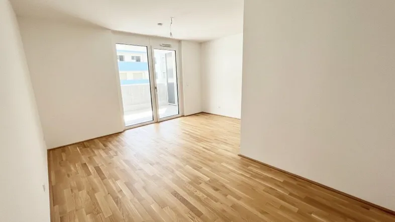 Helles, leeres Wohnzimmer mit Parkettboden und Zugang zu einem Balkon, ideal für neue Bewohner.