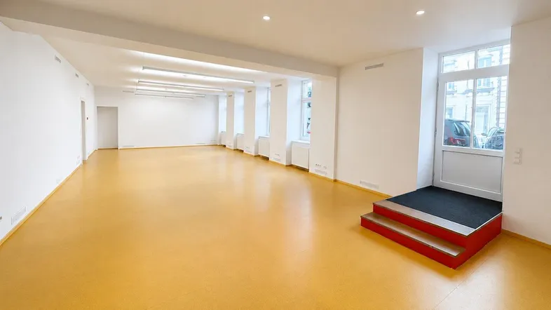 Großer, leerer Gewerberaum mit vielen Fenstern und hellem Linoleumboden, ideal für verschiedene Nutzungen.