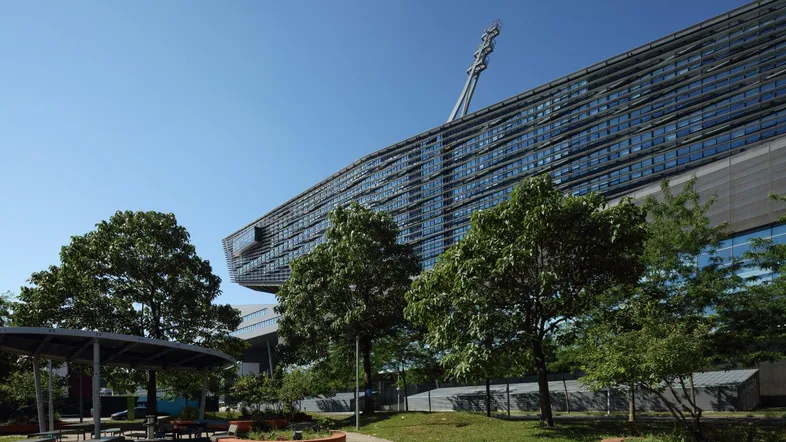 Modernes Bürogebäude mit markanter Architektur und Grünflächen im Vordergrund unter blauem Himmel.