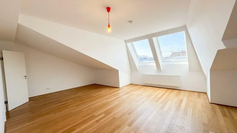 Heller Dachgeschossraum mit Holzboden und großen Dachfenstern, die viel Tageslicht hereinlassen.