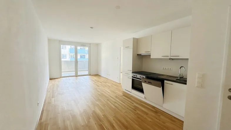 Heller, offener Wohnbereich mit integrierter Küchenzeile, Parkettboden und Zugang zum Balkon.