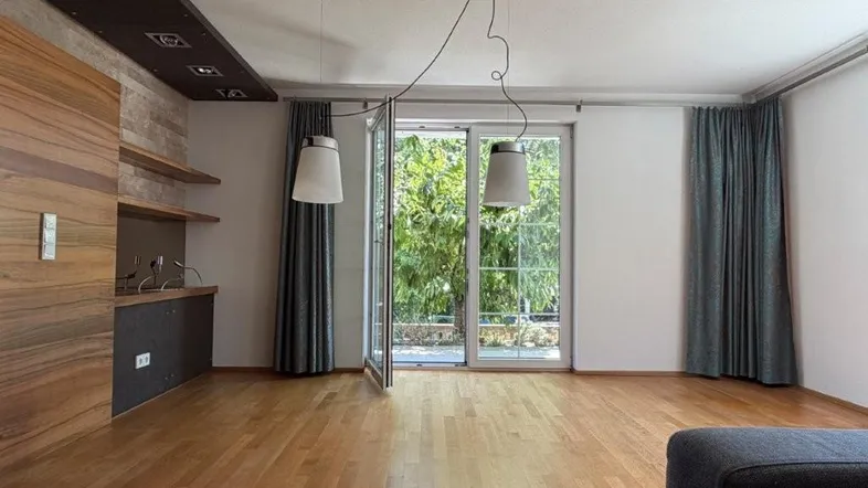 Helles Wohnzimmer mit Holzboden und Zugang zu einer Terrasse mit Blick ins Grüne.