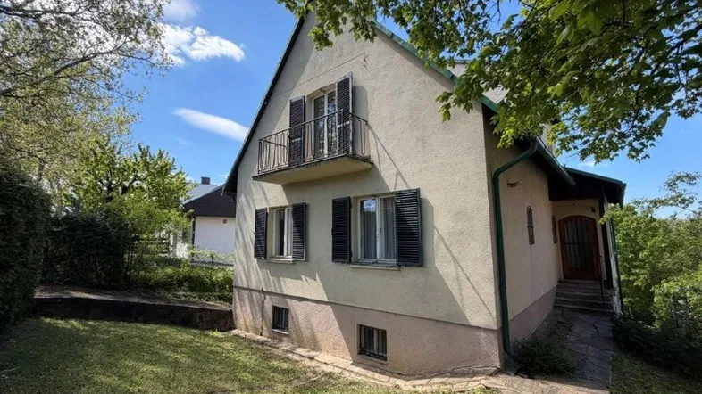 Klassisches Einfamilienhaus mit Balkon, Fensterläden und gepflegtem Vorgarten unter blauem Himmel.