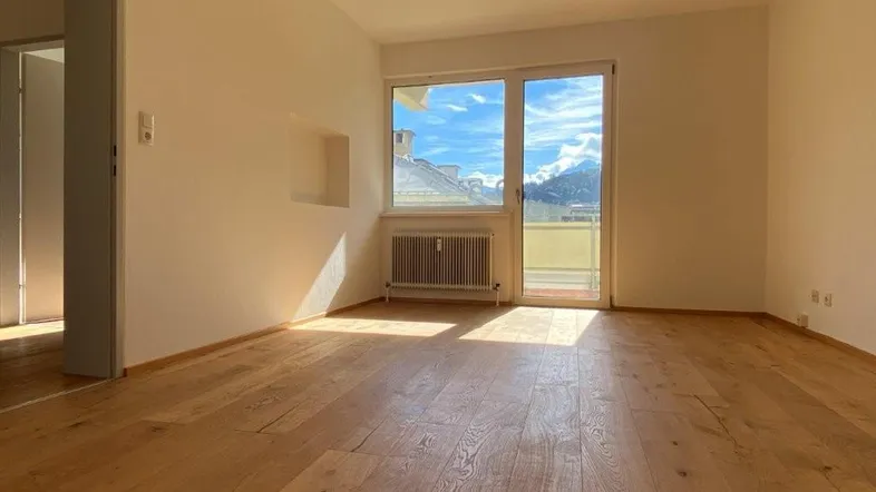 Helles Zimmer mit Holzboden, weißen Wänden und einem schönen Blick auf die Berge.
