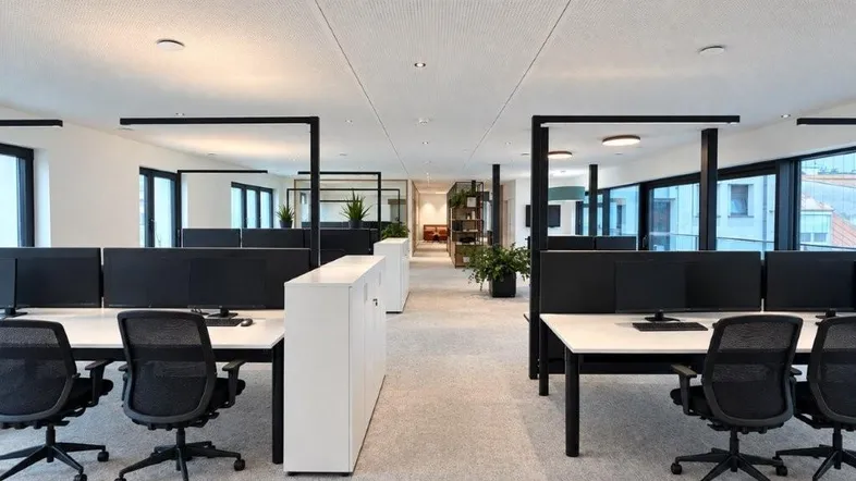Moderner Großraumbüro mit ergonomischen Arbeitsplätzen, Teppichboden und viel Tageslicht durch große Fenster.