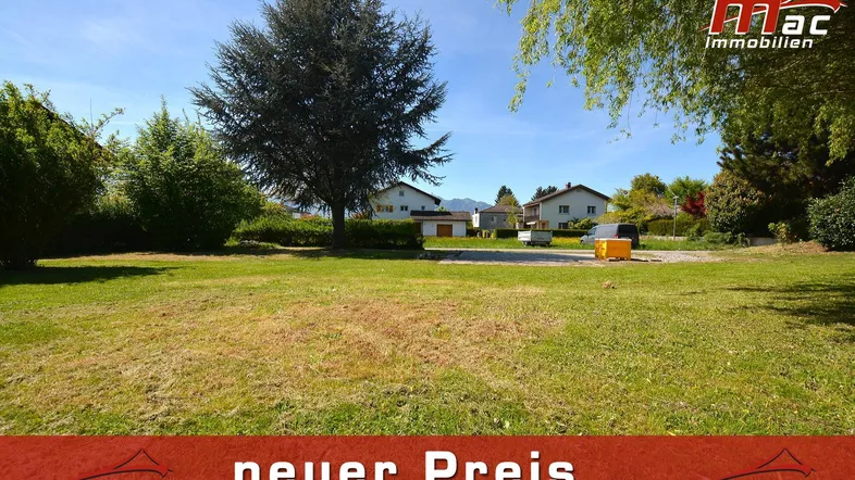 Große Rasenfläche mit Bäumen und Hecken, umgeben von Wohnhäusern und mit Bergblick im Hintergrund.