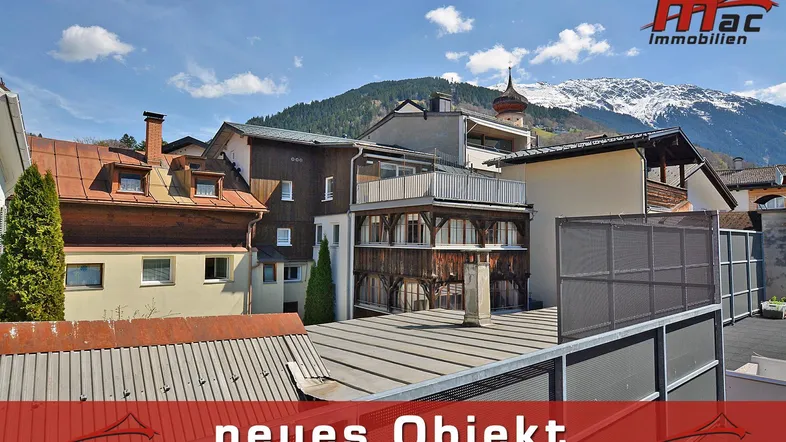 Blick auf die Gebäudefassade mit traditionellen Holzelementen und schneebedeckten Bergen im Hintergrund.