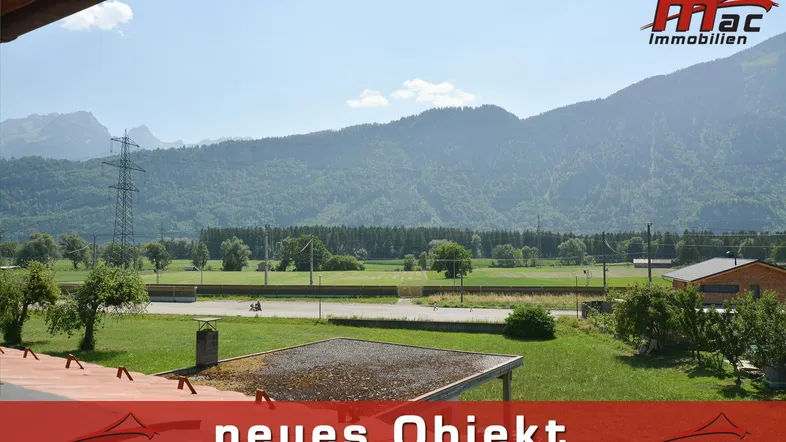 Weitläufiger Blick auf die umliegende Berglandschaft und grüne Felder unter blauem Himmel.