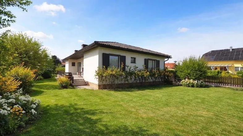 Freistehendes Einfamilienhaus mit großem, gepflegtem Rasen und blühenden Sträuchern unter blauem Himmel.
