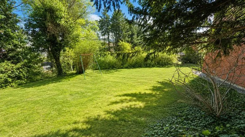 Gepflegter Garten mit Rasenfläche, Bäumen und einem Schaukelgestell unter blauem Himmel.