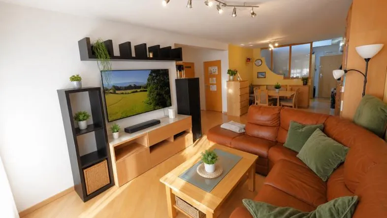 Helles Wohn- und Esszimmer mit bequemer Ledercouch, Holzboden und modernem Entertainment-Bereich.