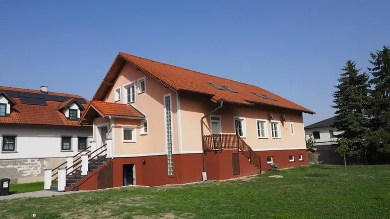 Haus mit orangefarbener Fassade und rotem Ziegeldach auf einem grünen Grundstück.