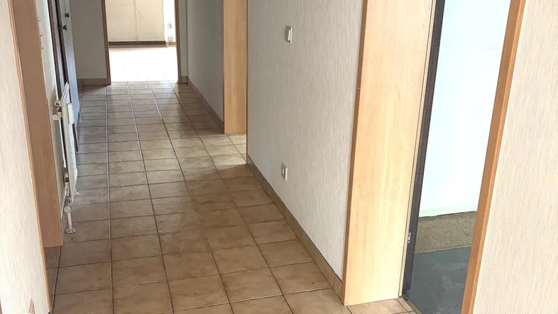 Langer Flur mit hellen Fliesen und mehreren Türen, der zu verschiedenen Räumen führt.