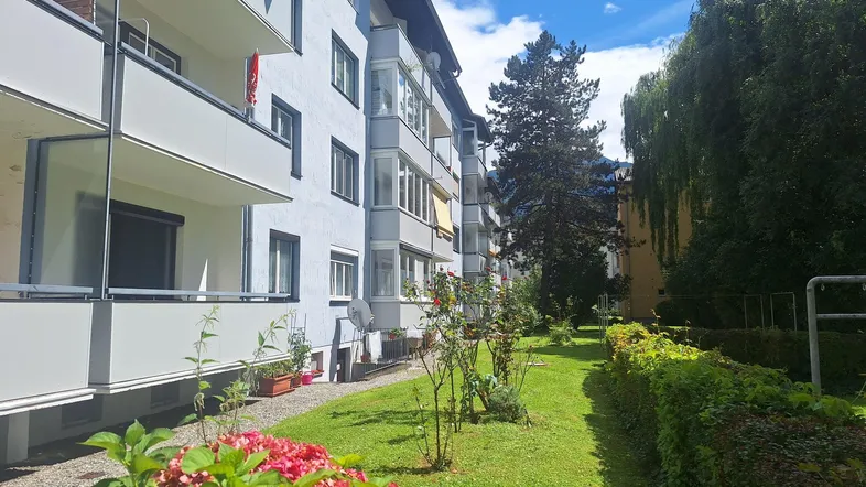 Mehrfamilienhaus mit gepflegtem Vorgarten und Balkonen unter blauem Himmel.