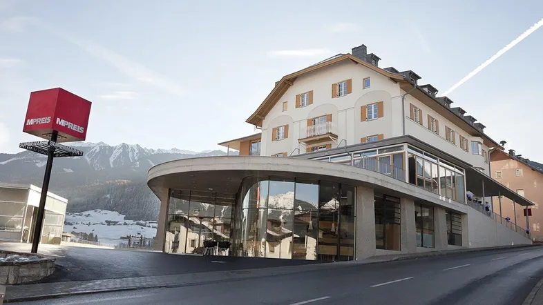 Modernes Gebäude mit geschwungener Glasfassade und traditionellem Dach vor einer Bergkulisse.