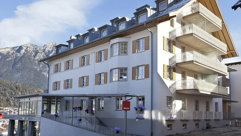 Modernes Gebäude mit mehreren Balkonen und Dachgauben vor einer beeindruckenden Bergkulisse.